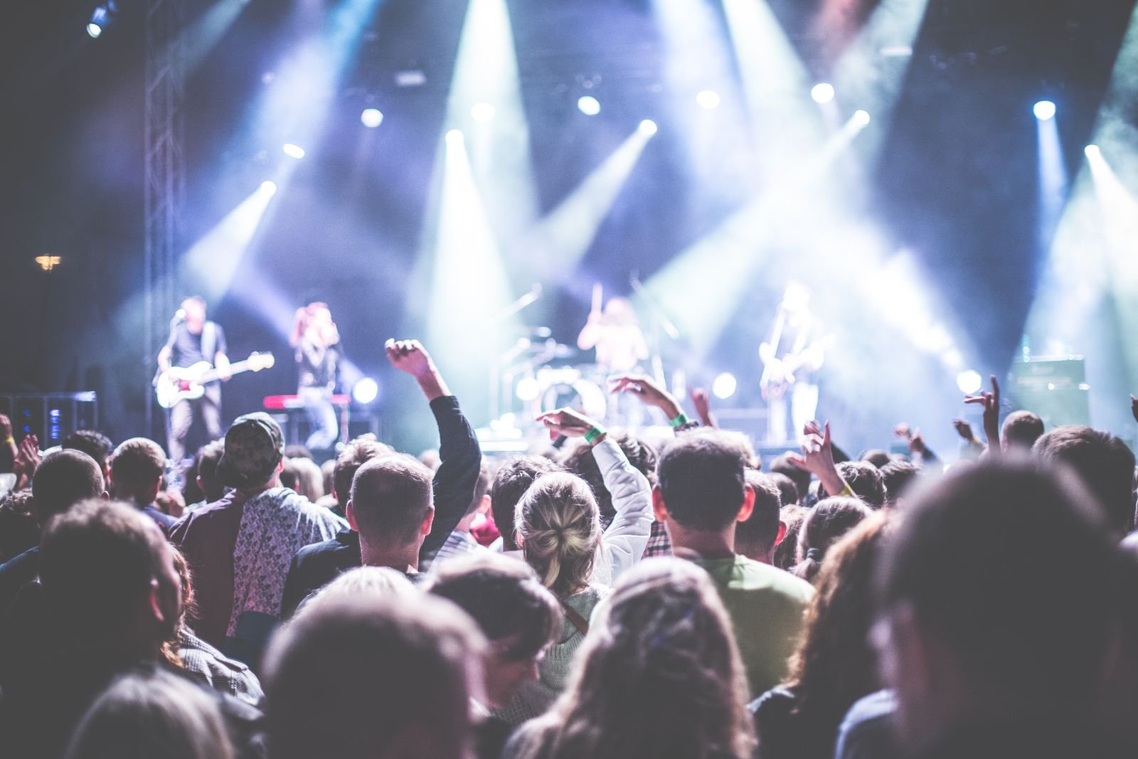 A packed concert crowd with hands raised under blue stage lights