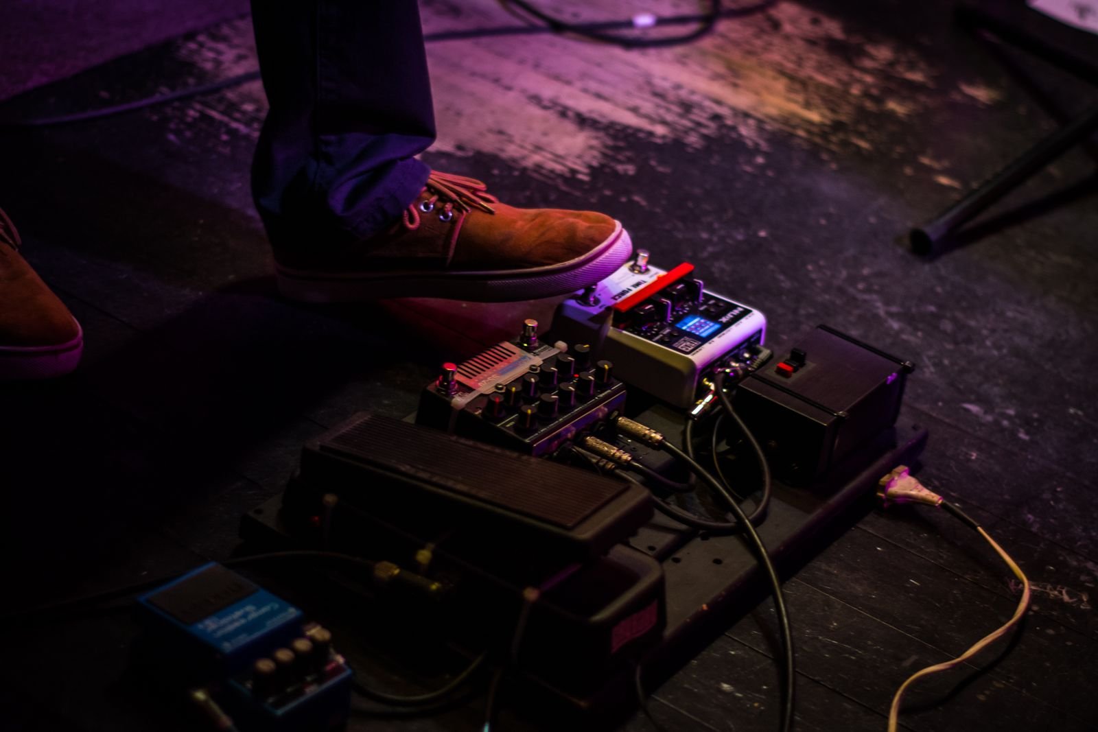 A guitar pedalboard wired up on a dark stage floor