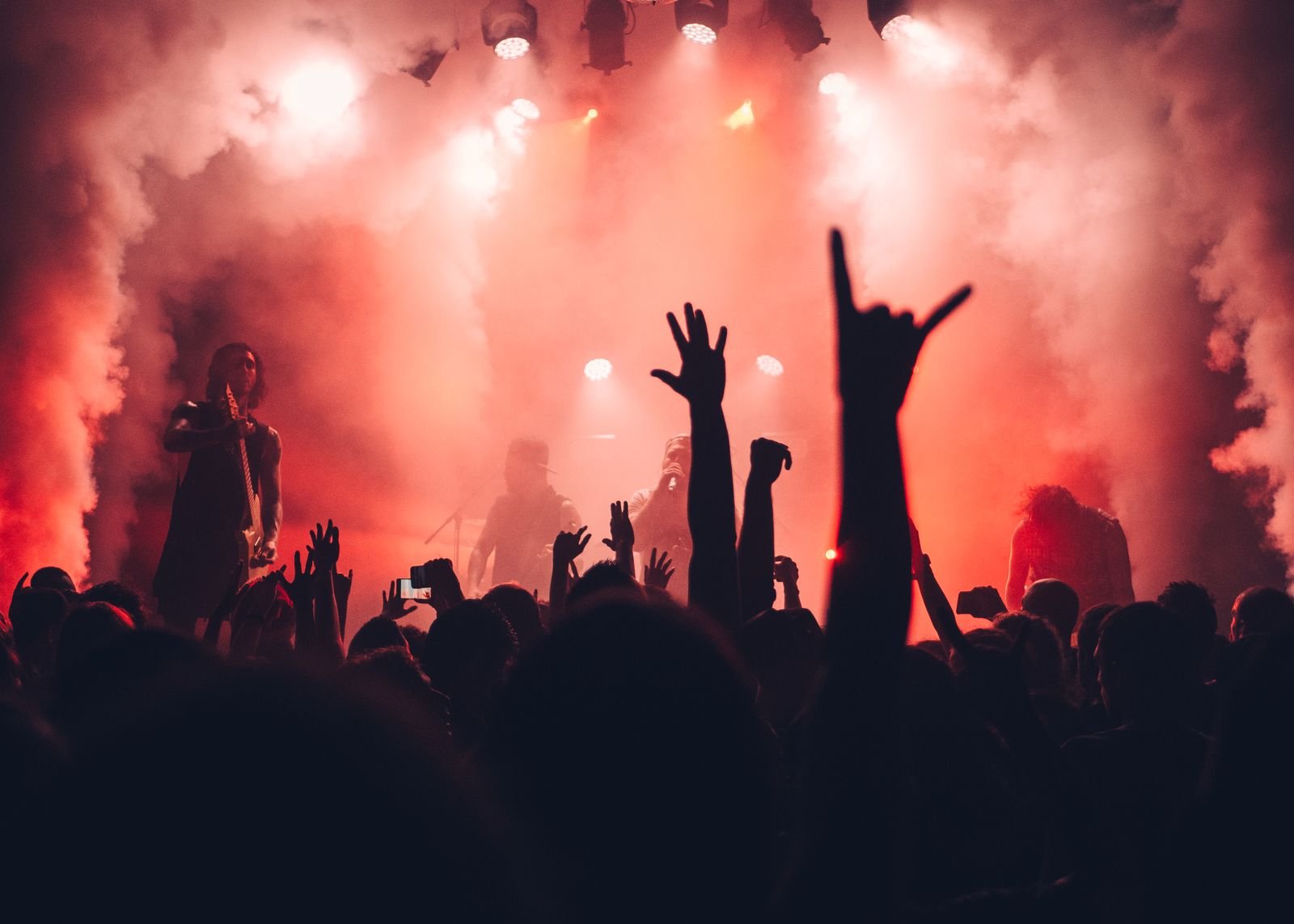 A red-lit live show with raised hands and rock-horn gestures