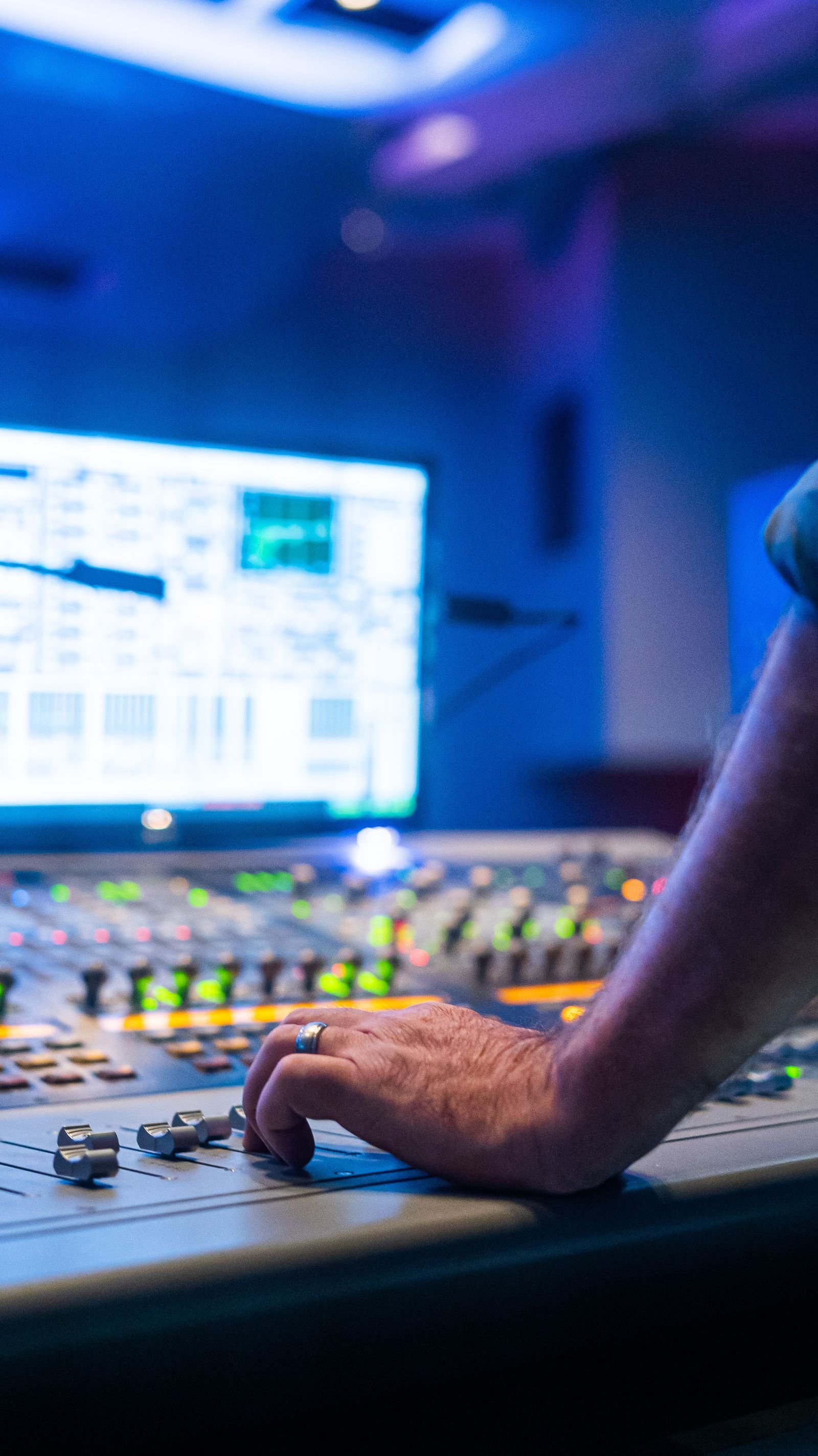 A hand resting on a mixing console fader bathed in blue studio light